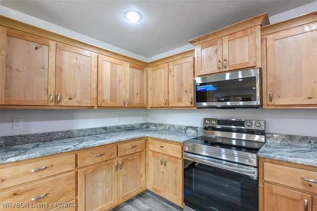 kitchen featuring appliances with stainless steel finishes, light hardwood / wood-style flooring, and light stone counters