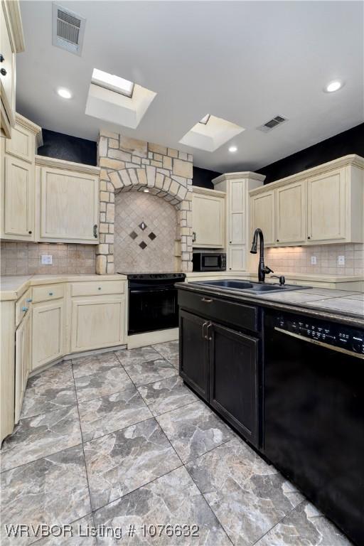 kitchen with a skylight, sink, backsplash, cream cabinets, and black appliances