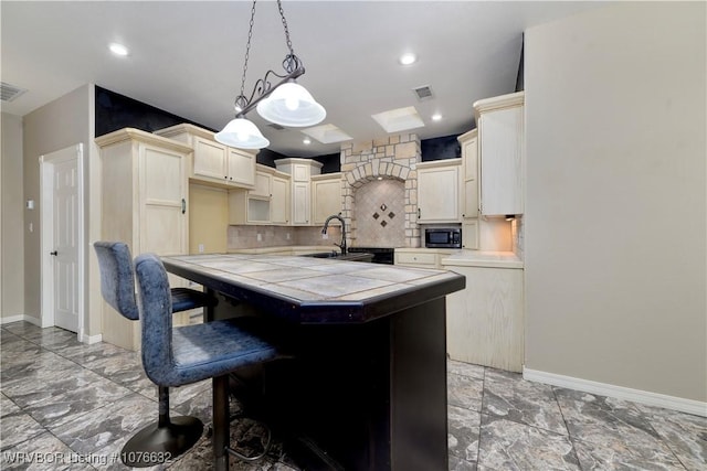 kitchen with tile countertops, cream cabinets, sink, hanging light fixtures, and decorative backsplash