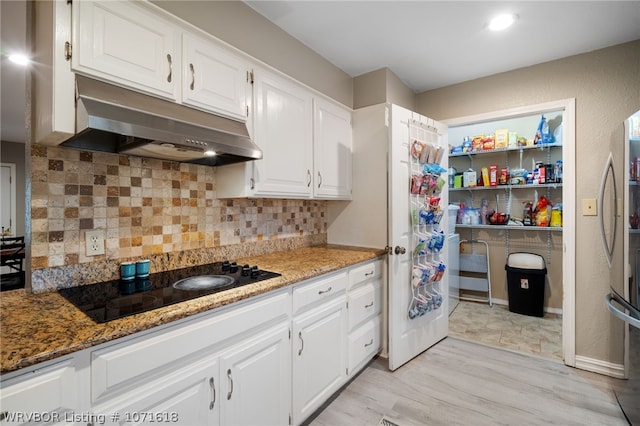 kitchen featuring decorative backsplash, dark stone countertops, black electric cooktop, white cabinetry, and stainless steel refrigerator