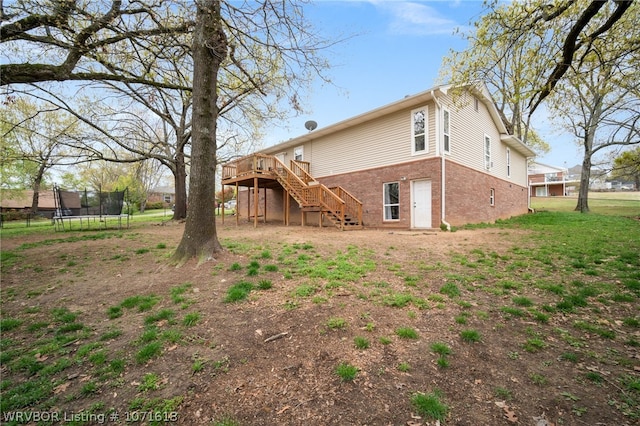 rear view of property featuring a lawn, a wooden deck, and a trampoline