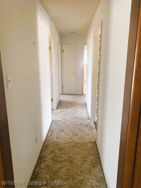 corridor with light carpet and a textured ceiling