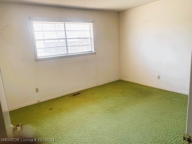 empty room with carpet, visible vents, a textured ceiling, and baseboards