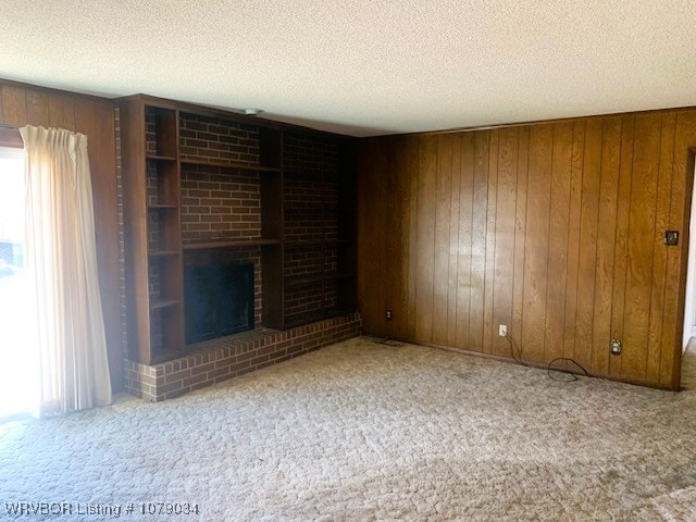 unfurnished living room featuring a textured ceiling, carpet floors, a fireplace, and wooden walls