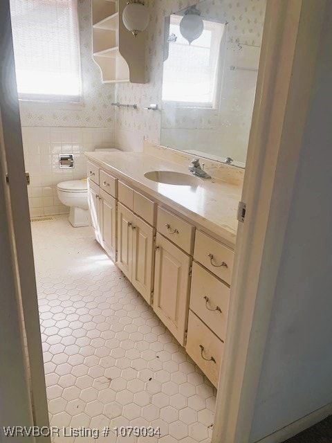 bathroom featuring toilet, wallpapered walls, tile walls, and vanity