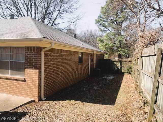 view of side of home with brick siding, roof with shingles, and a fenced backyard