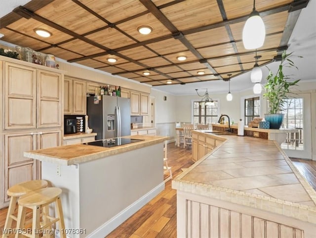 kitchen with hanging light fixtures, light brown cabinets, wooden ceiling, stainless steel fridge, and black electric stovetop