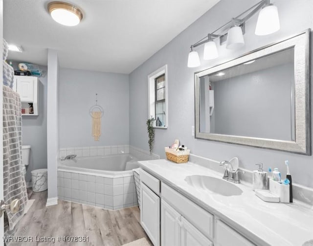 bathroom with vanity, hardwood / wood-style flooring, tiled bath, and toilet