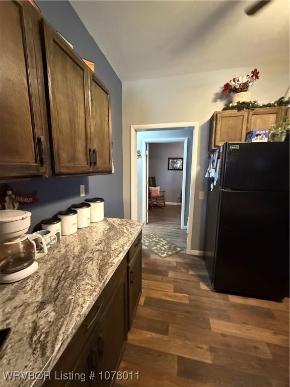 kitchen with light stone countertops, black fridge, and dark wood-type flooring