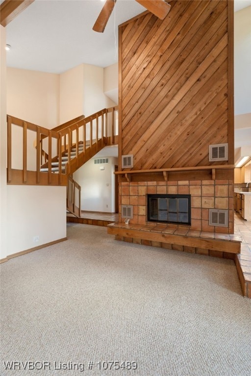 unfurnished living room featuring ceiling fan, wooden walls, beamed ceiling, light carpet, and a fireplace