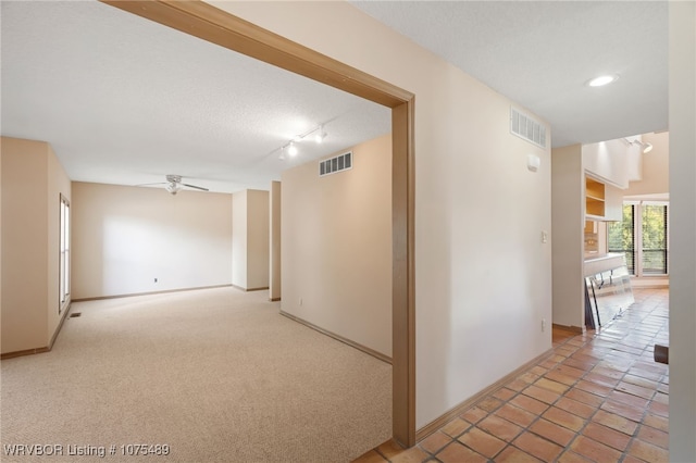 hallway with a textured ceiling, rail lighting, and light carpet