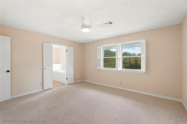 unfurnished bedroom with carpet, ceiling fan, a textured ceiling, and ensuite bath