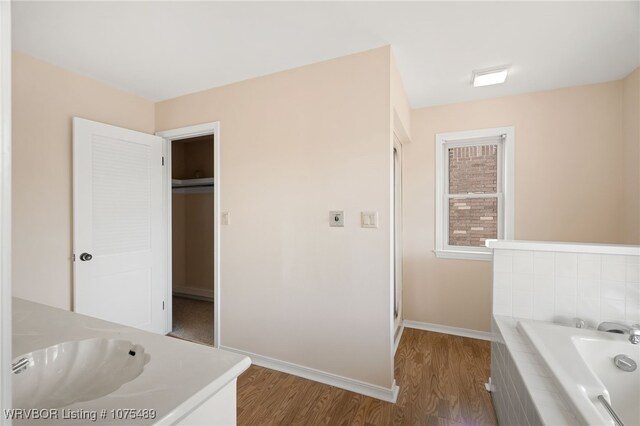 bathroom featuring hardwood / wood-style flooring, a relaxing tiled tub, and sink