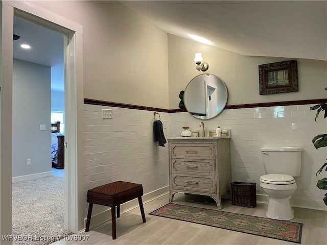 bathroom featuring wood-type flooring, vanity, toilet, and tile walls