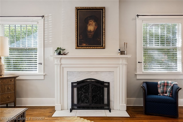 living area with a high end fireplace, a healthy amount of sunlight, and hardwood / wood-style flooring