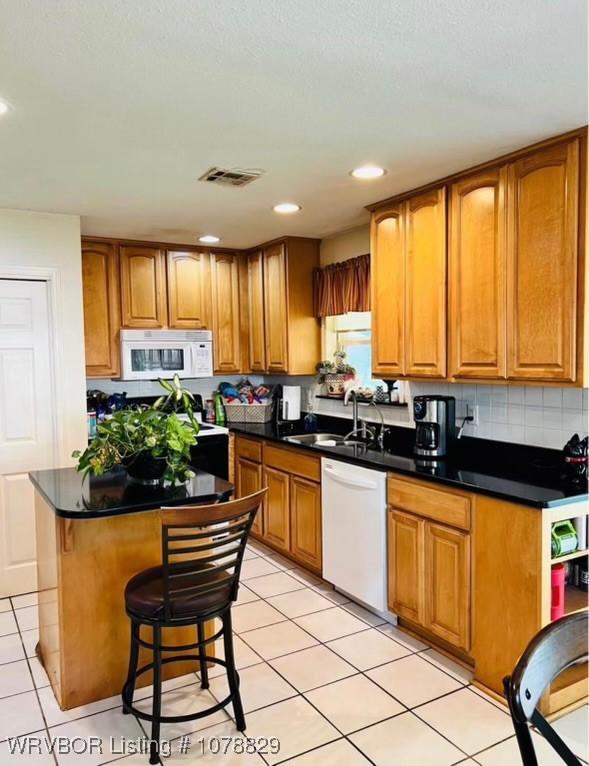 kitchen featuring sink, a breakfast bar area, tasteful backsplash, a center island, and white appliances