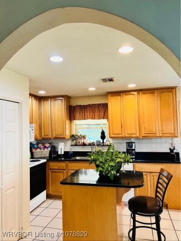 kitchen featuring light tile patterned floors, range with electric stovetop, a center island, and a breakfast bar