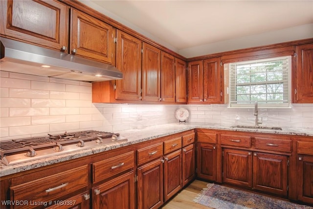 kitchen featuring tasteful backsplash, a sink, stainless steel gas cooktop, under cabinet range hood, and light stone countertops