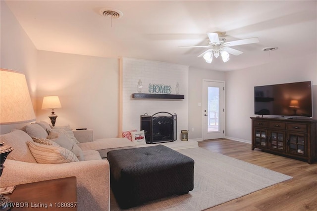 living room with a ceiling fan, wood finished floors, baseboards, a brick fireplace, and visible vents