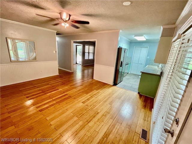 2119 55th Pl, Fort Smith, AR 72904 - unfurnished living room featuring light wood-style floors, a textured ceiling, a wainscoted wall, ornamental molding, and a ceiling fan