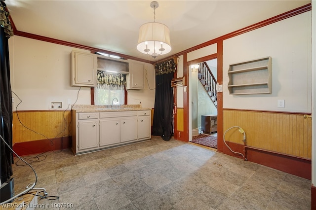 kitchen featuring sink, hanging light fixtures, crown molding, and wood walls