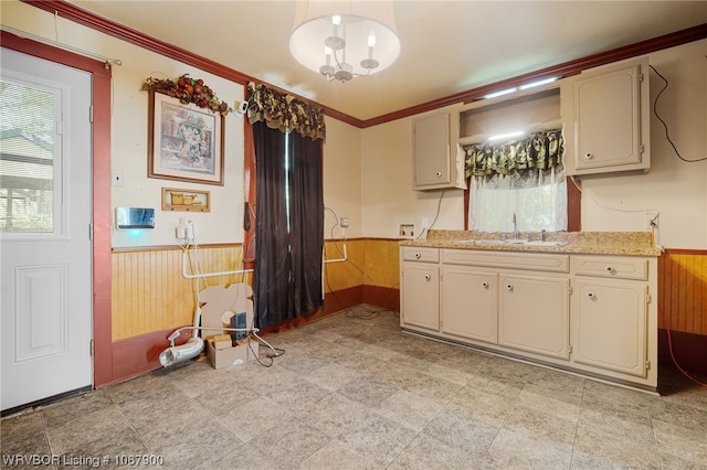 kitchen with ornamental molding, wooden walls, sink, pendant lighting, and cream cabinetry