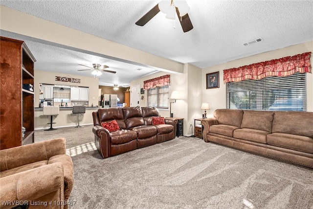 living room featuring carpet flooring, a ceiling fan, visible vents, and a wealth of natural light