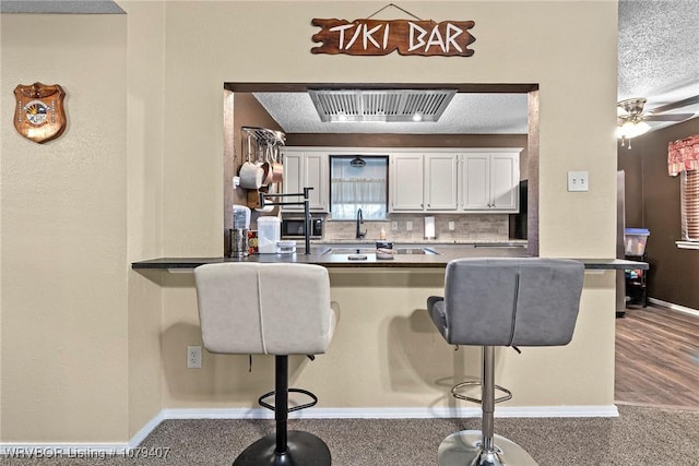 kitchen with visible vents, a textured ceiling, a peninsula, and a breakfast bar area