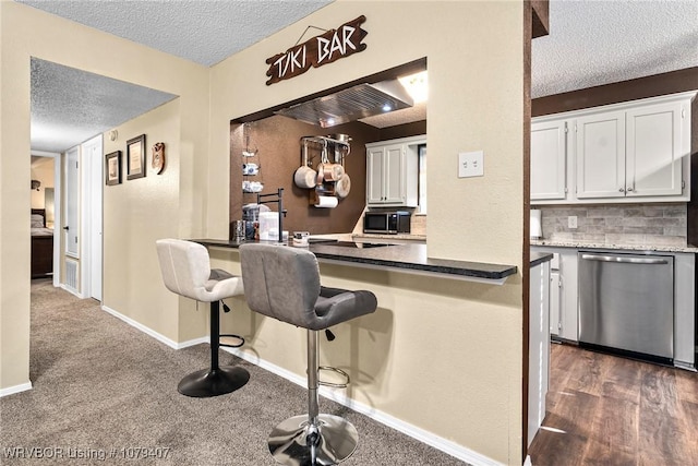 kitchen with tasteful backsplash, a textured ceiling, white cabinets, baseboards, and dishwasher