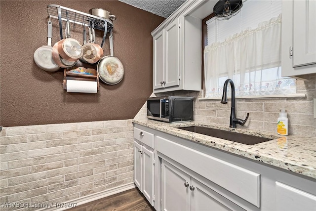 kitchen featuring white cabinets, a textured wall, dark wood-style flooring, and a sink