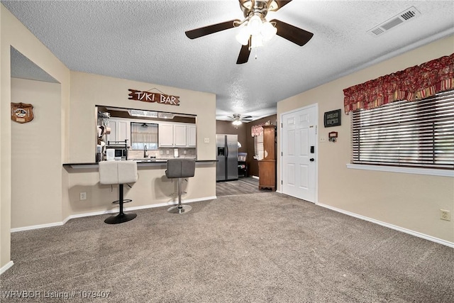 interior space featuring visible vents, a breakfast bar, a ceiling fan, stainless steel fridge, and carpet floors