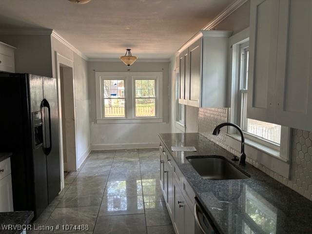 kitchen featuring black refrigerator with ice dispenser, dark stone counters, crown molding, sink, and white cabinetry