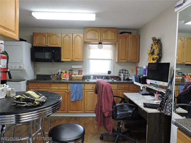 kitchen with stacked washer and dryer, black microwave, a sink, and wood finished floors