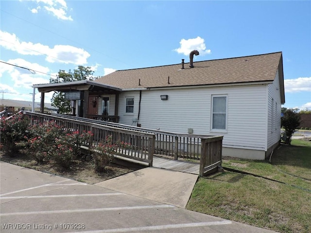 view of front of house featuring a shingled roof, a front lawn, and a deck