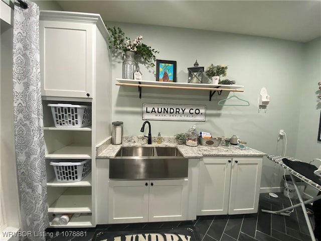 bar featuring light stone countertops, sink, and white cabinets