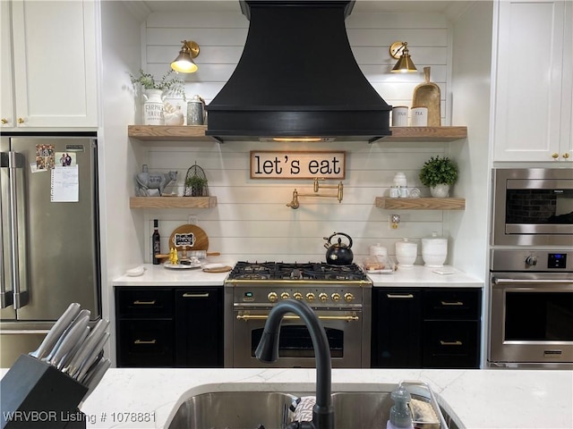 kitchen featuring light stone countertops, custom range hood, white cabinets, and premium appliances