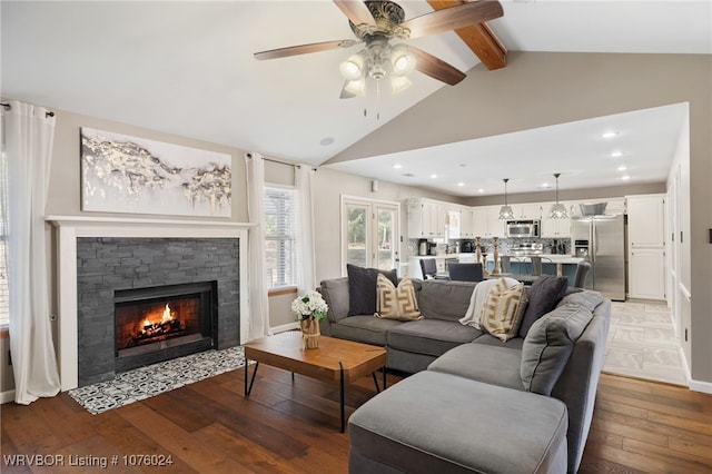 living room with hardwood / wood-style floors, ceiling fan, lofted ceiling with beams, and a stone fireplace