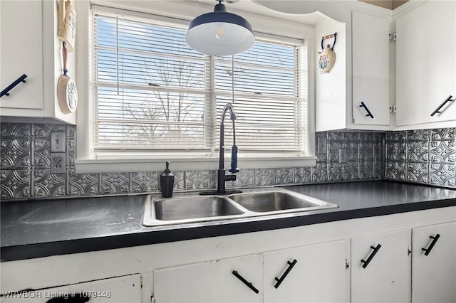 kitchen featuring tasteful backsplash, dark countertops, white cabinets, and a sink