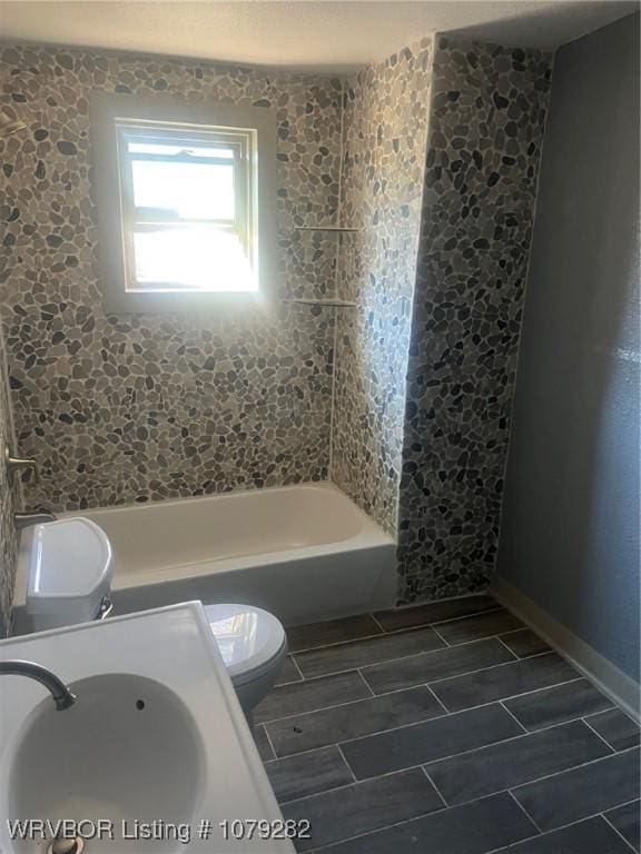 full bath with wood finish floors, bathtub / shower combination, toilet, a sink, and baseboards