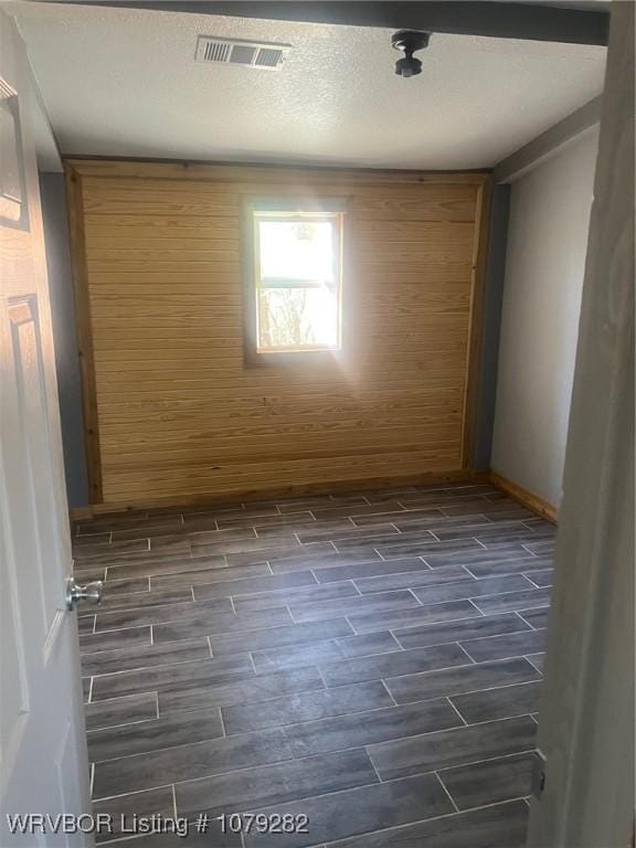 empty room featuring a textured ceiling, wood finish floors, visible vents, and baseboards