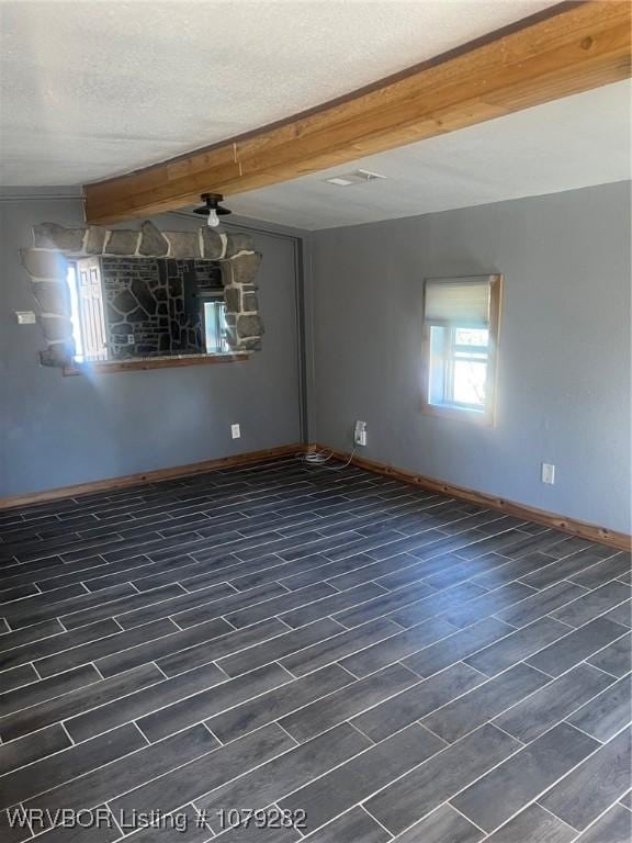 unfurnished room with dark wood-style floors, a textured ceiling, baseboards, and beam ceiling