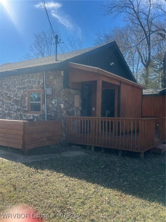 rear view of house with stone siding, a yard, and a deck