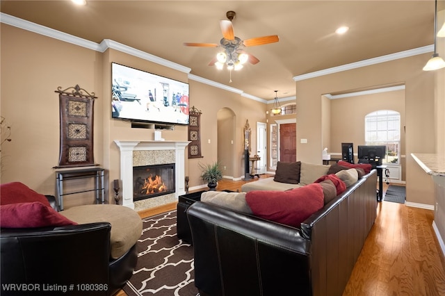living area featuring wood finished floors, a ceiling fan, ornamental molding, arched walkways, and a glass covered fireplace