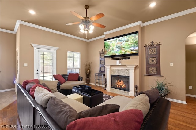 living area featuring arched walkways, baseboards, a glass covered fireplace, a ceiling fan, and wood finished floors