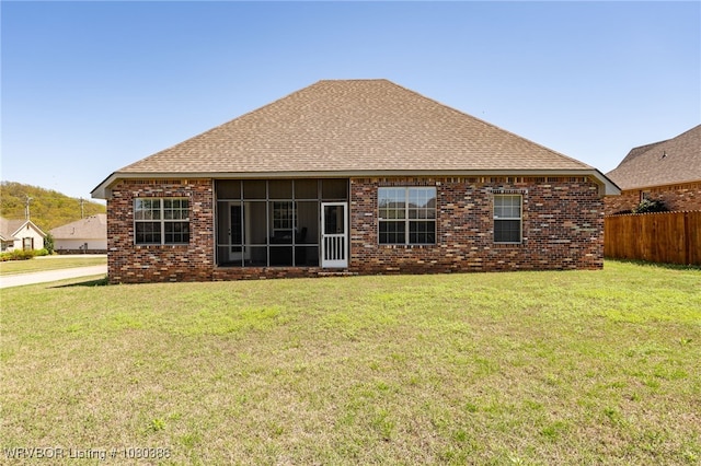 rear view of property featuring fence, a lawn, a shingled roof, and brick siding