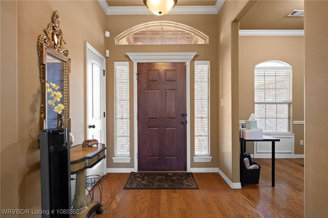 entrance foyer with baseboards, wood finished floors, visible vents, and ornamental molding