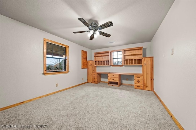 unfurnished office featuring light carpet, built in desk, plenty of natural light, and ceiling fan