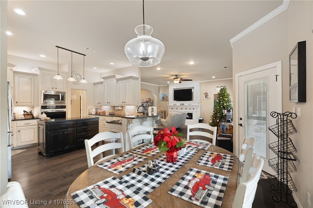 dining room featuring crown molding, ceiling fan, a fireplace, and dark wood-type flooring