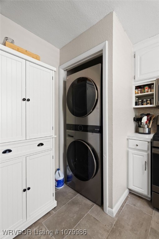 clothes washing area featuring a textured ceiling, stacked washer / dryer, baseboards, laundry area, and light tile patterned floors