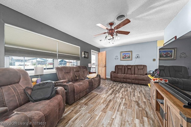 living room with visible vents, light wood-style floors, ceiling fan, and a textured ceiling
